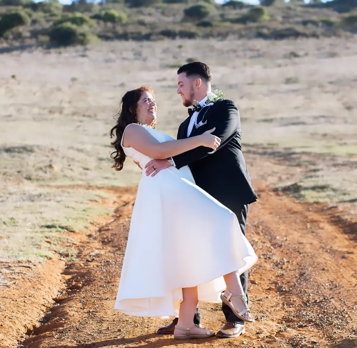 Couple embracing on a dirt track in an open field during a couple shoot
