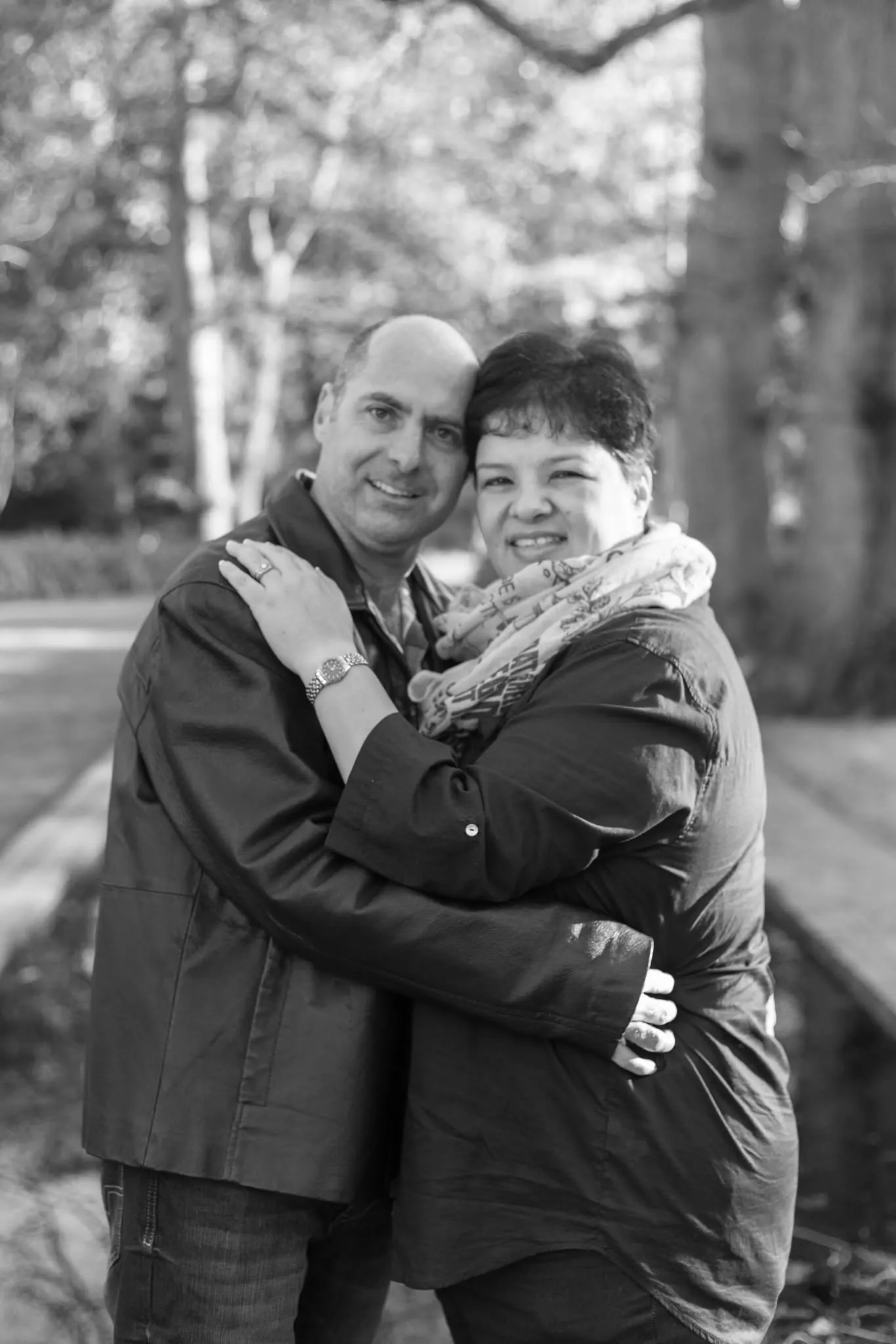 Black and white portrait of a smiling couple hugging under trees.