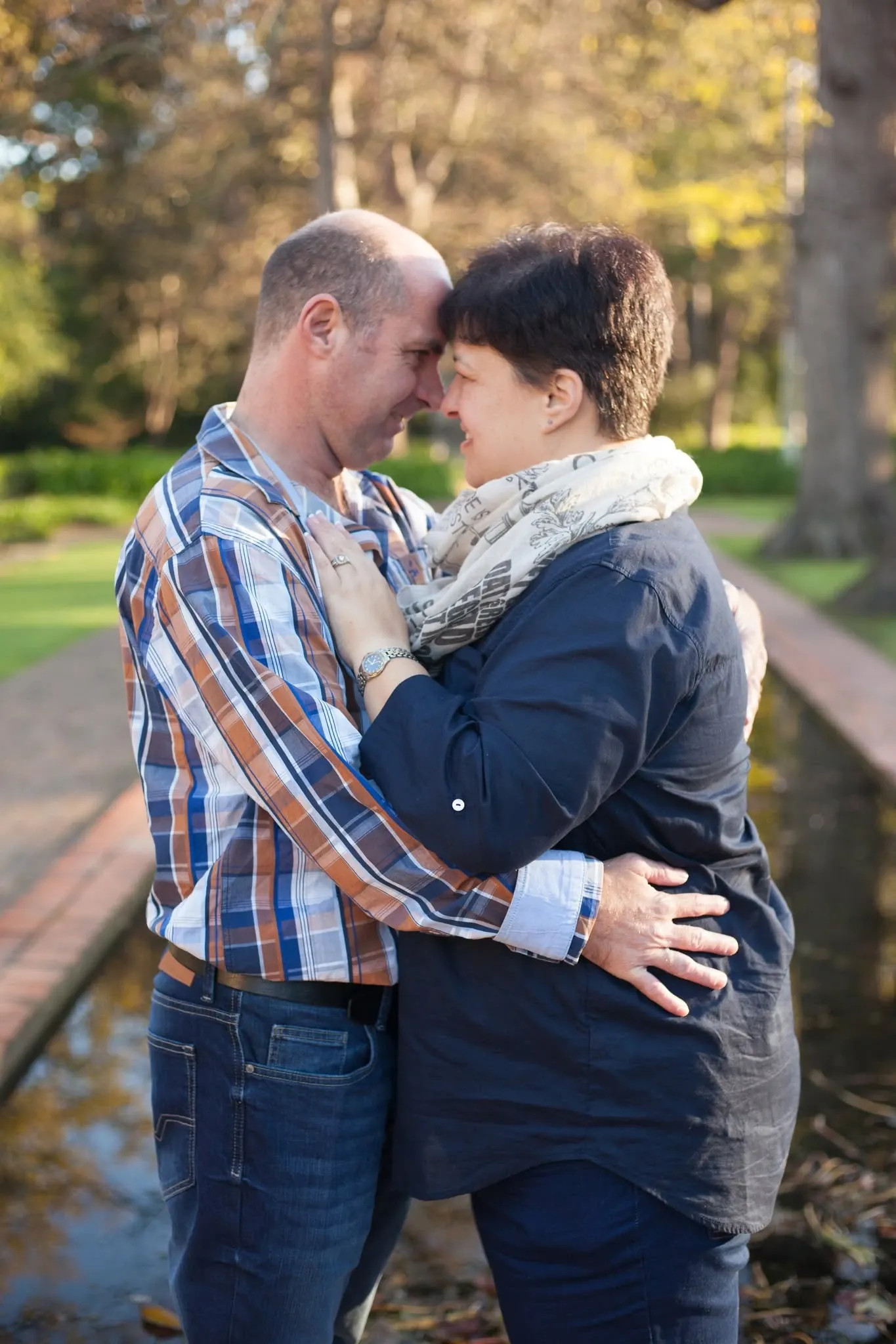 Couple embracing on a garden path, foreheads touching, in soft afternoon light.