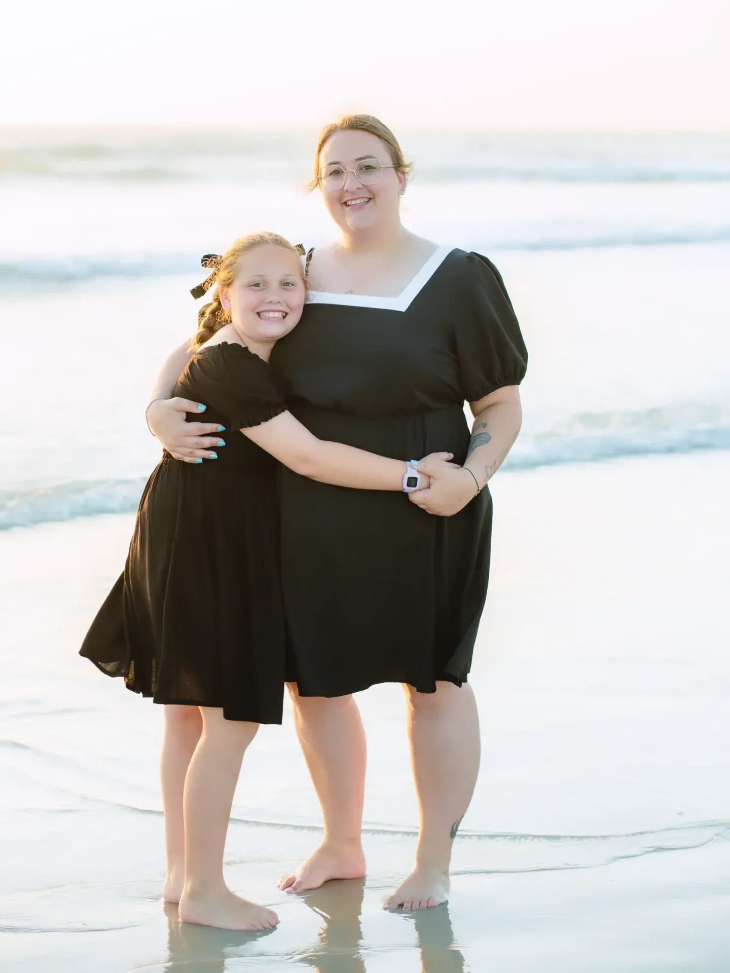Mother and daughter hugging barefoot in the shallow water during a family beach photoshoot