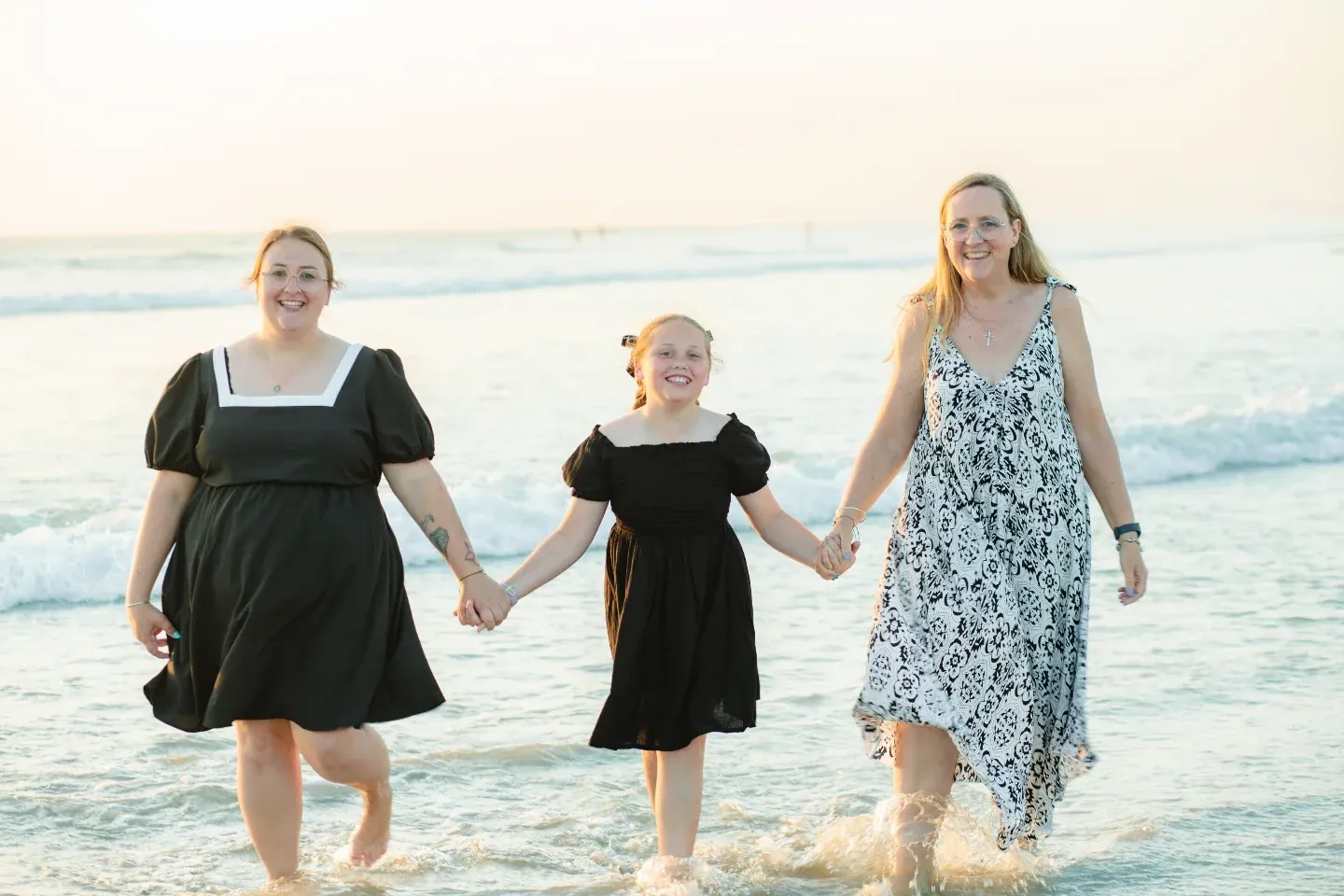Three family members walking hand in hand through the shallows at a beach photoshoot