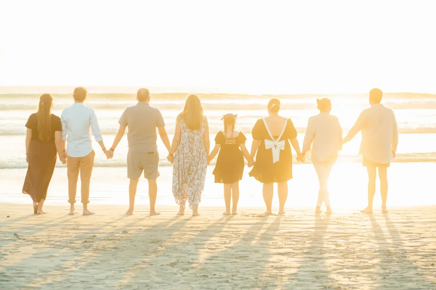 Backlit family walking hand in hand along the beach towards the setting sun