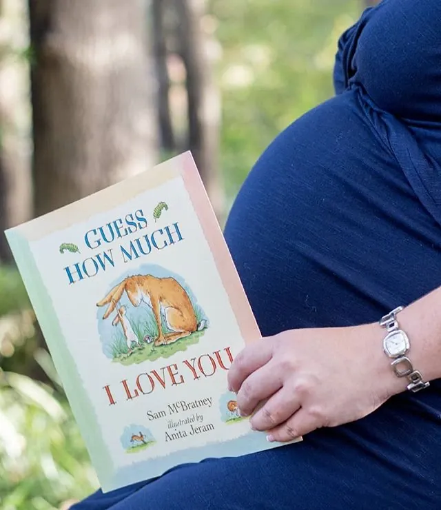 Maternity photoshoot detail: the children's book Guess How Much I Love You held against the bump