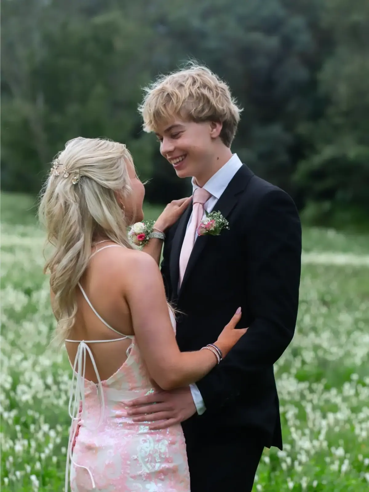 Matric dance couple in a pink sequin gown and black suit smiling at each other in a field of flowers
