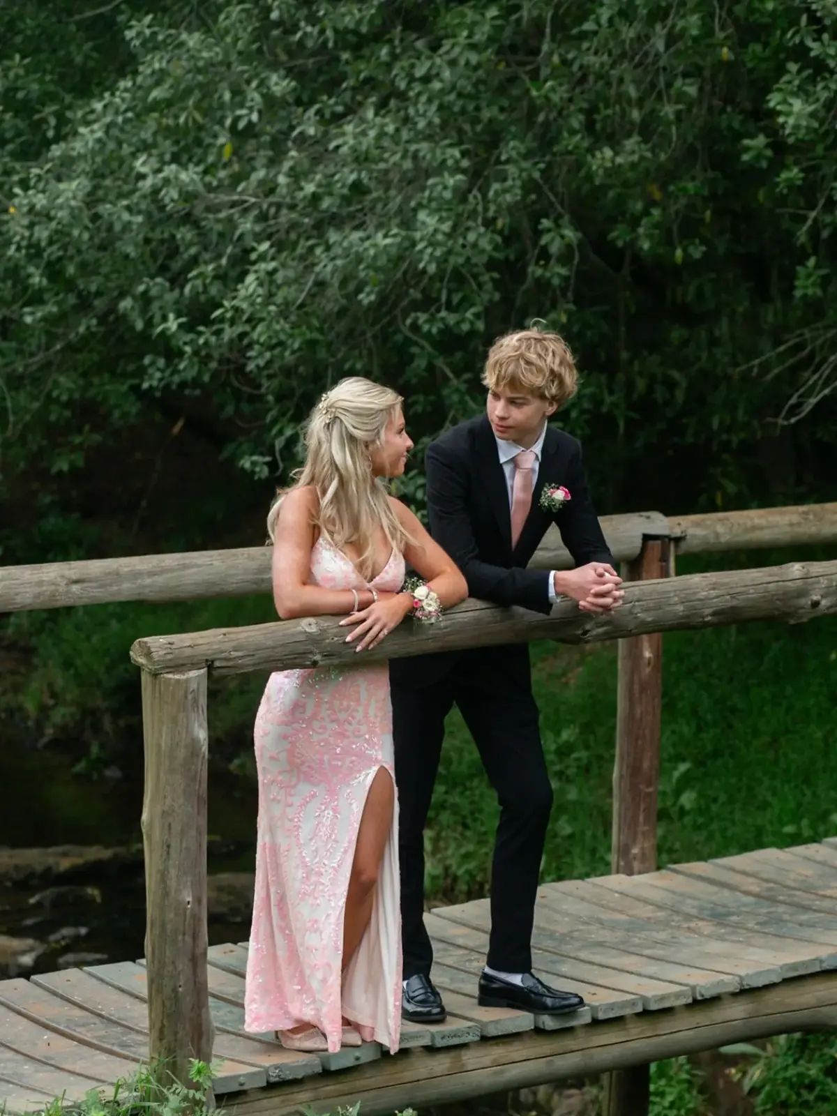 Matric dance couple leaning on a rustic wooden bridge railing