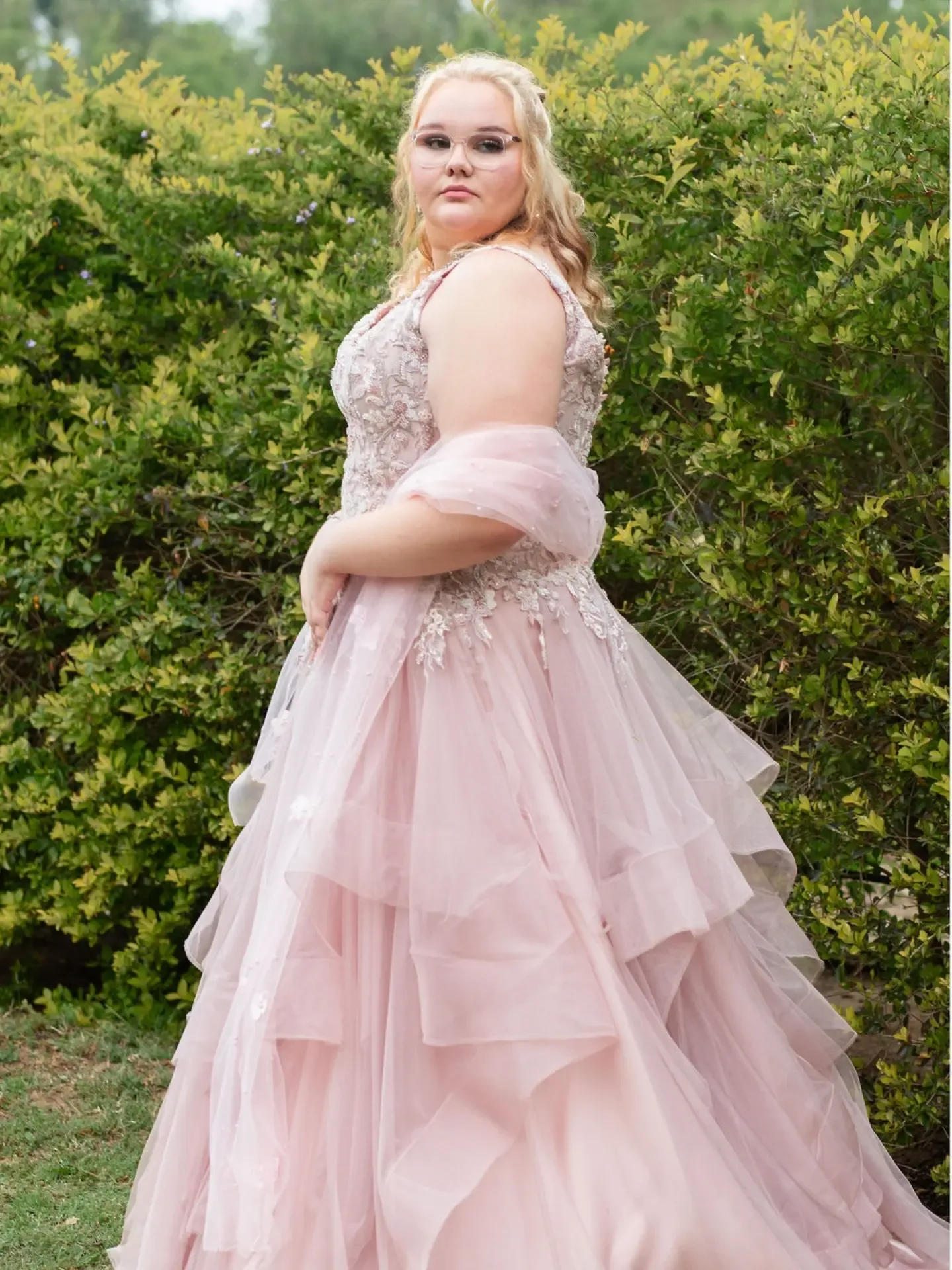 Side-on matric dance portrait against green shrubs, showing the gown's beaded bodice.