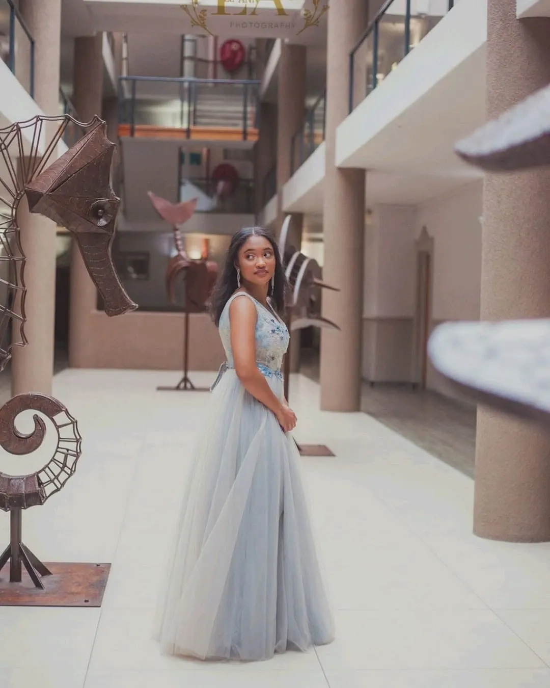 Matriculant in a grey tulle gown looking back over her shoulder in a sculptural atrium