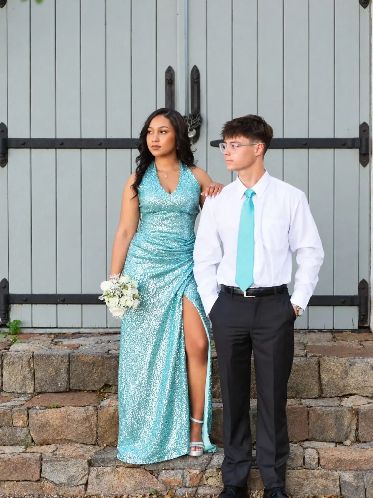 Matric farewell couple in a teal sequin dress and matching teal tie in front of a grey barn door.