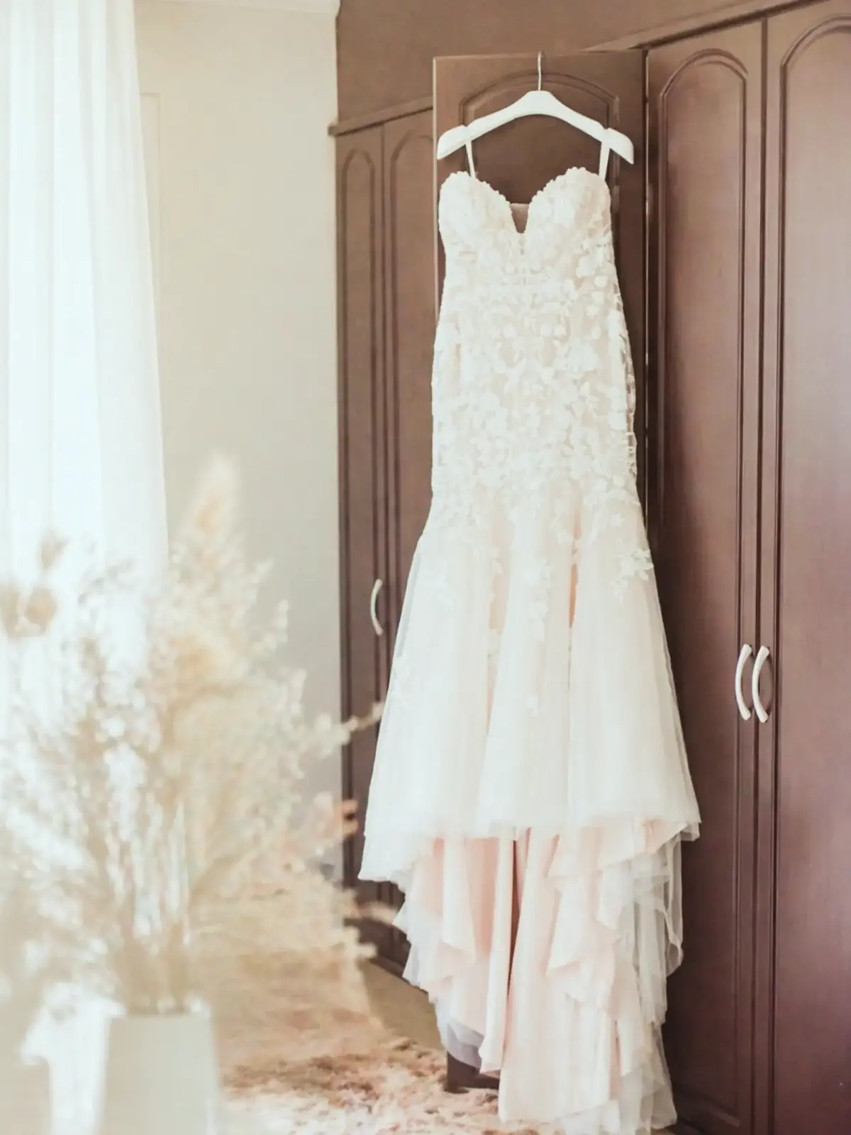 Lace wedding dress hanging on a wardrobe door while the bride gets ready