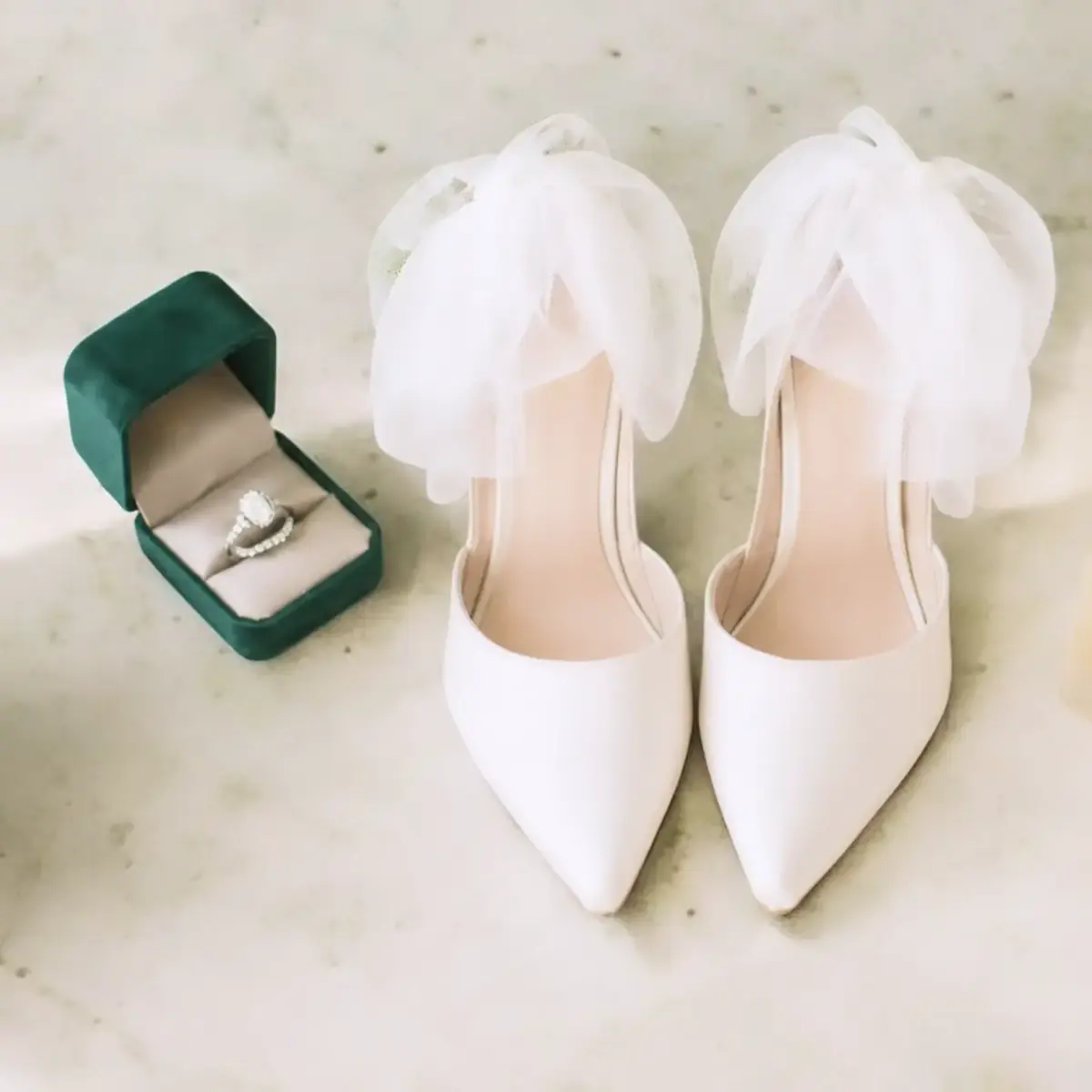 Wedding details: engagement ring in a green velvet box beside white bridal shoes with tulle bows